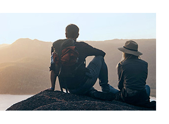 Man and woman hikers resting on rock, overlooking vista of coastal hills in the distance